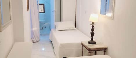A hotel room with two beds, a bedside table with a lamp, a wardrobe, and a bathroom visible through an open door.