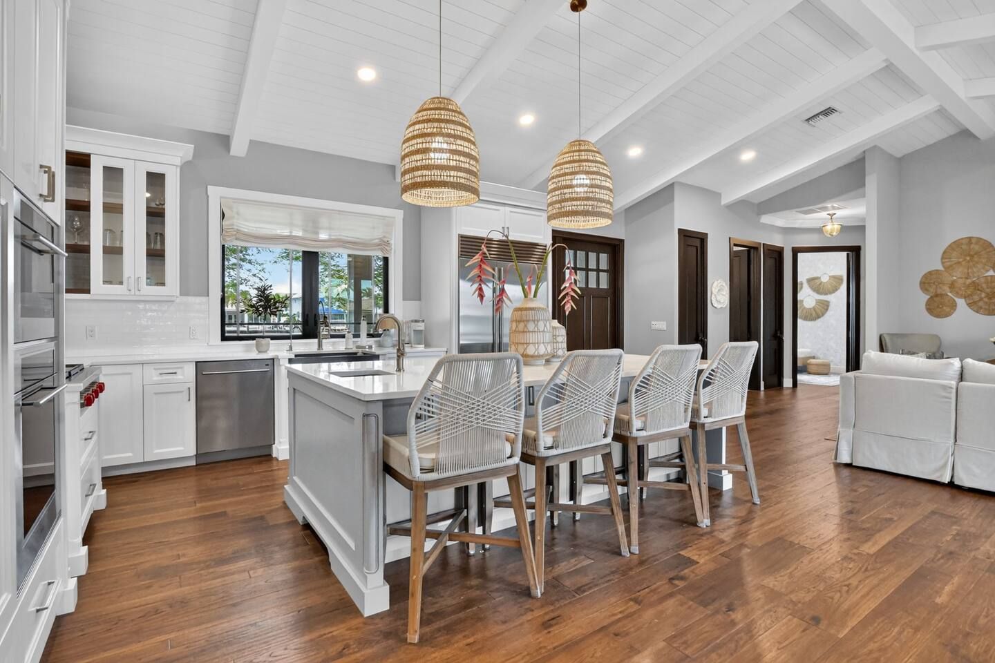 A modern kitchen with white cabinetry, a central island, and a dining area with wicker chairs.