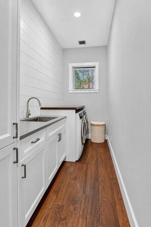 A compact laundry room with a washing machine, a sink, and a window. - The Boynton Boat House (Boynton Beach)