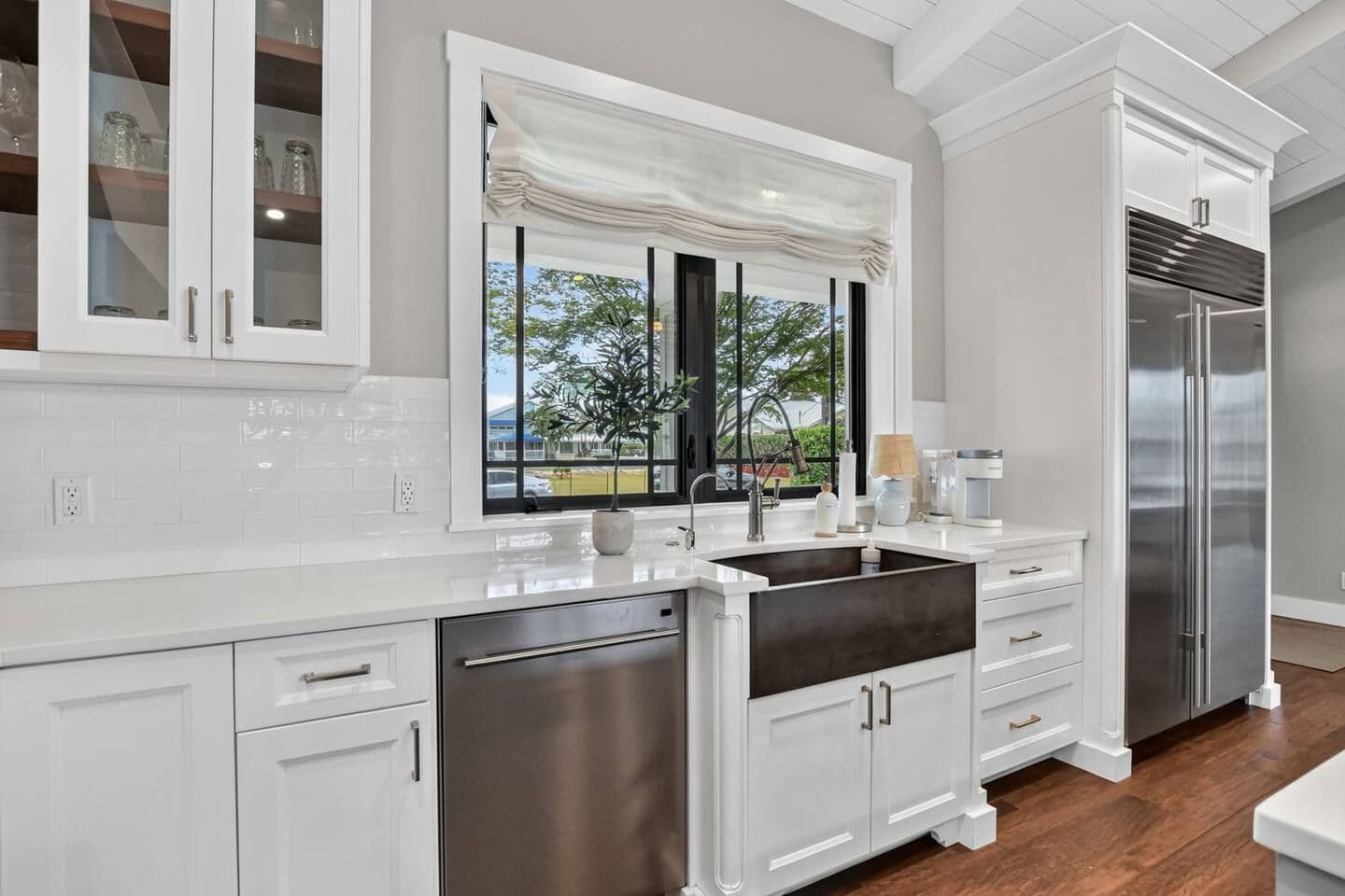 A modern kitchen with white cabinetry, a stainless steel refrigerator, and a window with a view of greenery.
