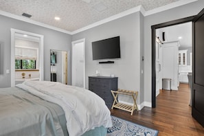 A bedroom with a bed, dresser, television, and a view of the bathroom. - The Boynton Boat House (Boynton Beach)