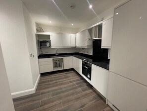 A compact kitchen with white cabinets, a black countertop, and a microwave. - Entire Luxury 2 Bedroom Apartment, Free Parking. (South Croydon)