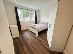 A bedroom with a bed, a wardrobe, a radiator, and a window with curtains. - Entire Luxury 2 Bedroom Apartment, Free Parking. (South Croydon)