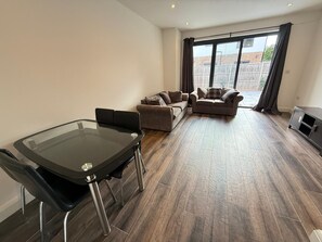 A modern living room with a glass dining table, two sofas, and a dark wood floor. - Entire Luxury 2 Bedroom Apartment, Free Parking. (South Croydon)