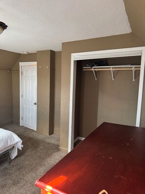 Ein Schlafzimmer mit einem Bett, einem Holzschrank, einem Kleiderschrank mit Kleiderstange und einer Tür.