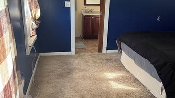 A bedroom with a bed, carpeted floor, and a bathroom visible through an open door.