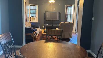 A dining area with a round table, four chairs, a ceiling fan, and a television in the background.