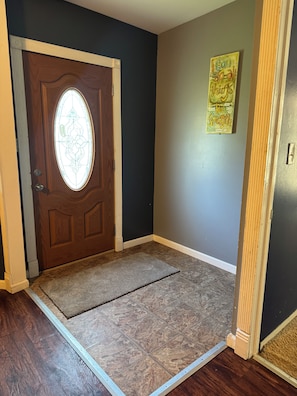 A room with a wooden door, a doormat, a wall with a motivational quote, and a floor with a patterned tile design.