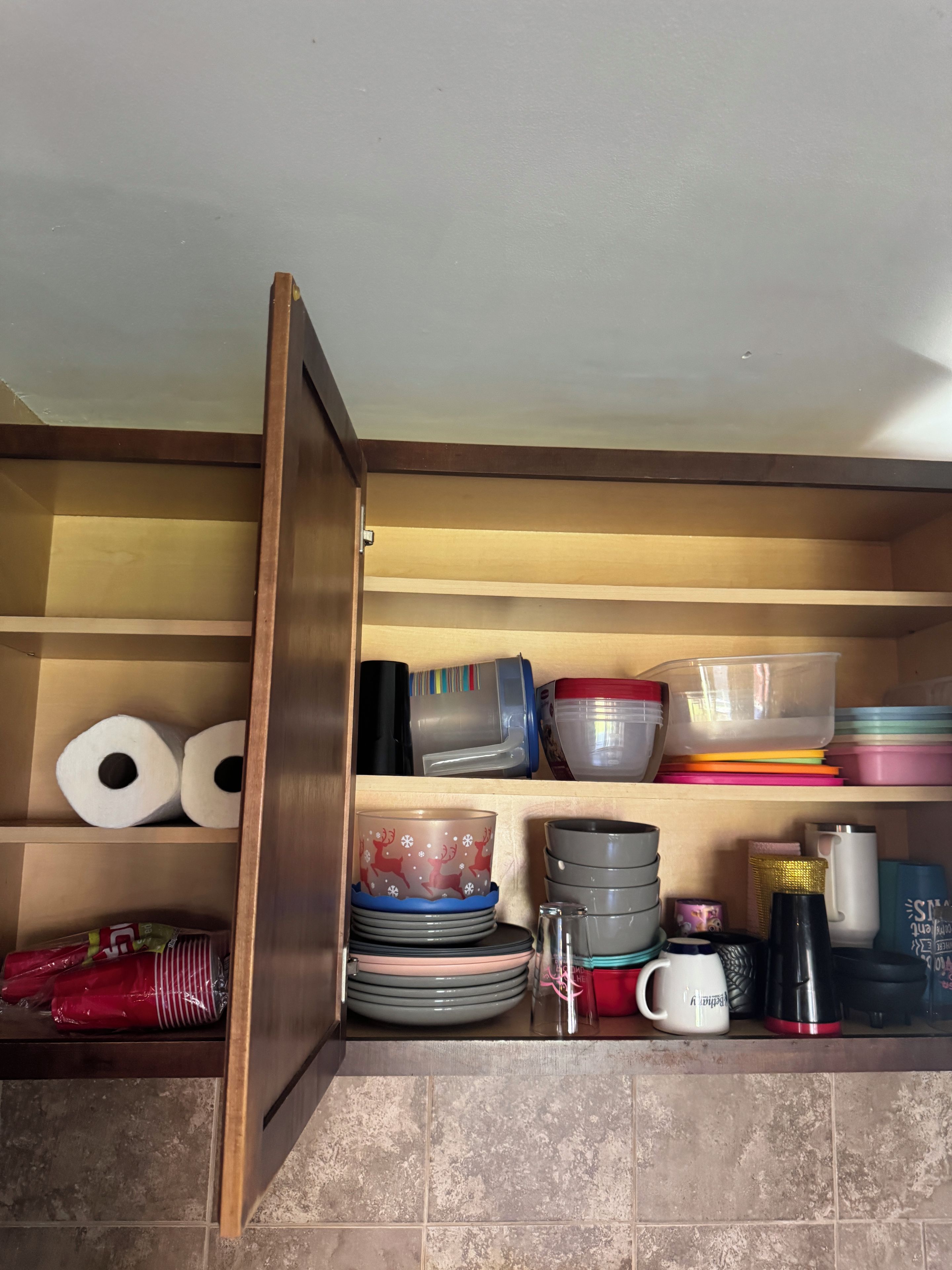 A kitchen cabinet with shelves containing various kitchenware, including plates, bowls, and a coffee maker.