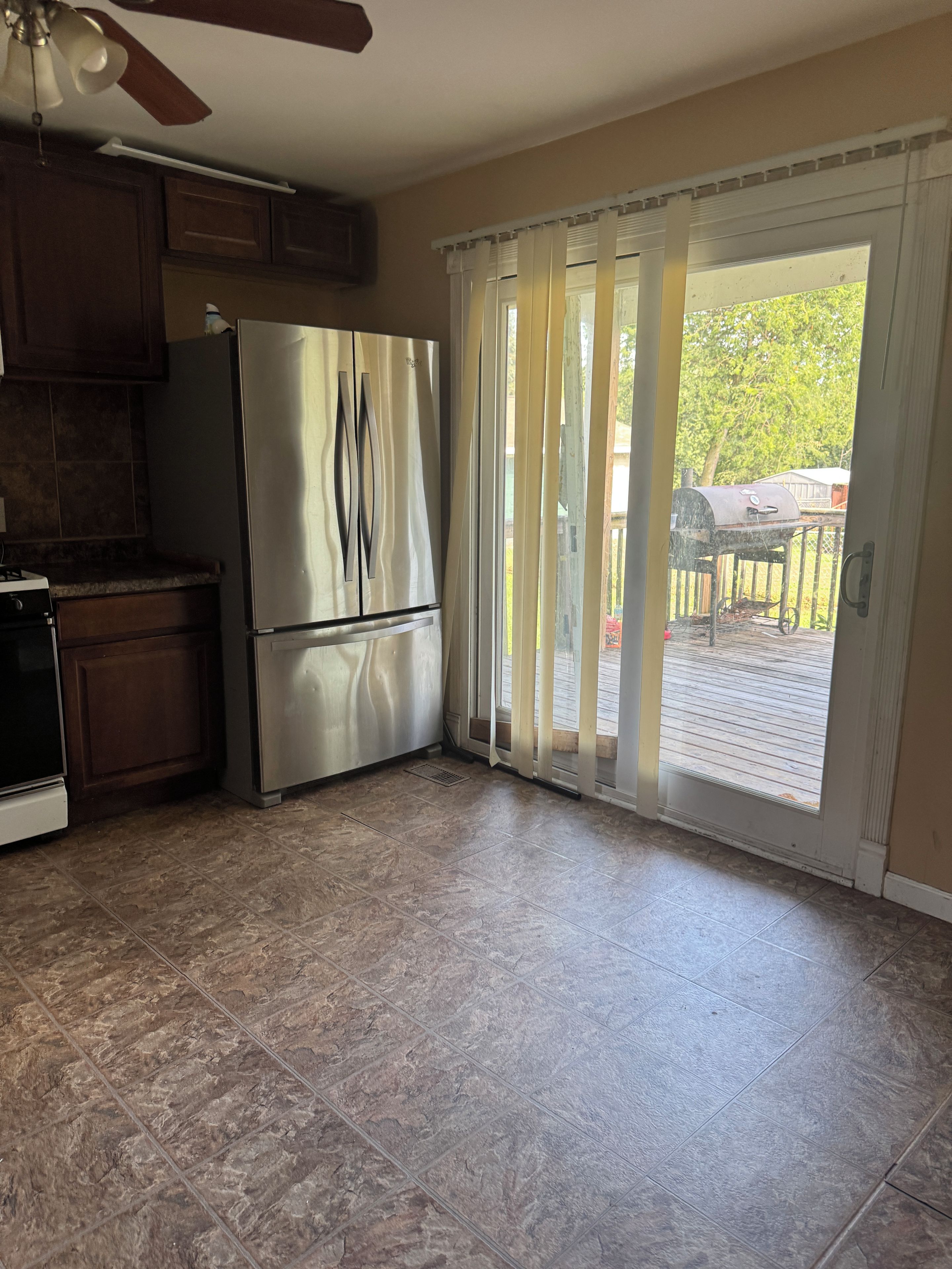 Una cocina con un refrigerador de acero inoxidable, un ventilador de techo y un patio con puerta corrediza de vidrio.