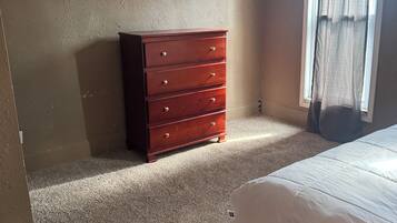 A bedroom with a bed, a wooden dresser, and a window with curtains.