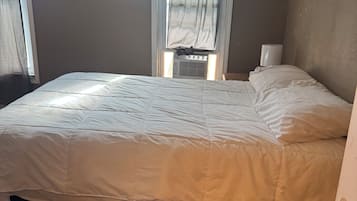 Une chambre à coucher avec un lit, une fenêtre avec des rideaux, un radiateur et une porte.