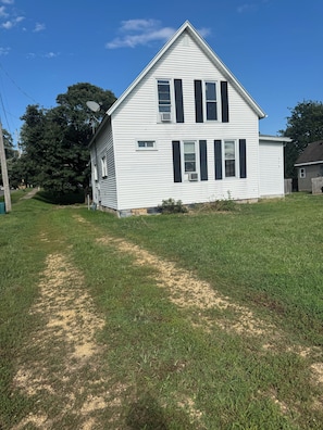 A two-story house with a grassy yard and a paved path leading to the front door.