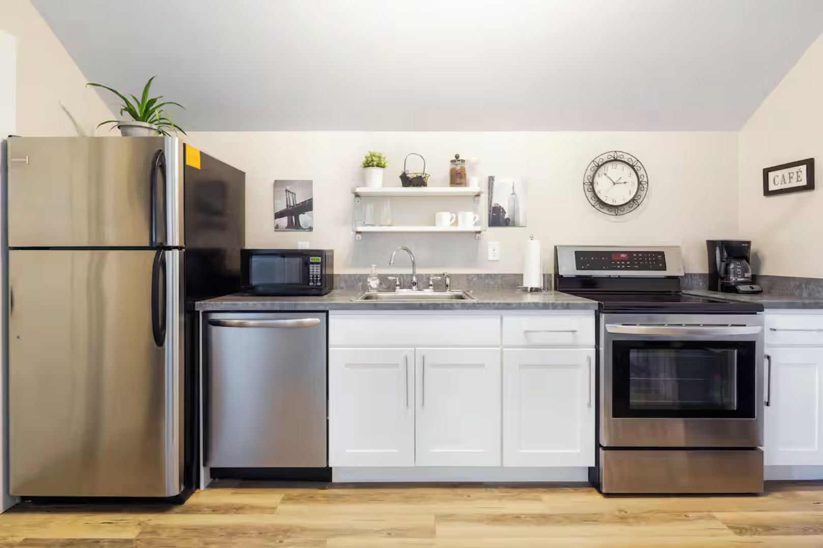 Una cucina moderna con elettrodomestici in acciaio inossidabile, mobili bianchi e pavimento in legno.