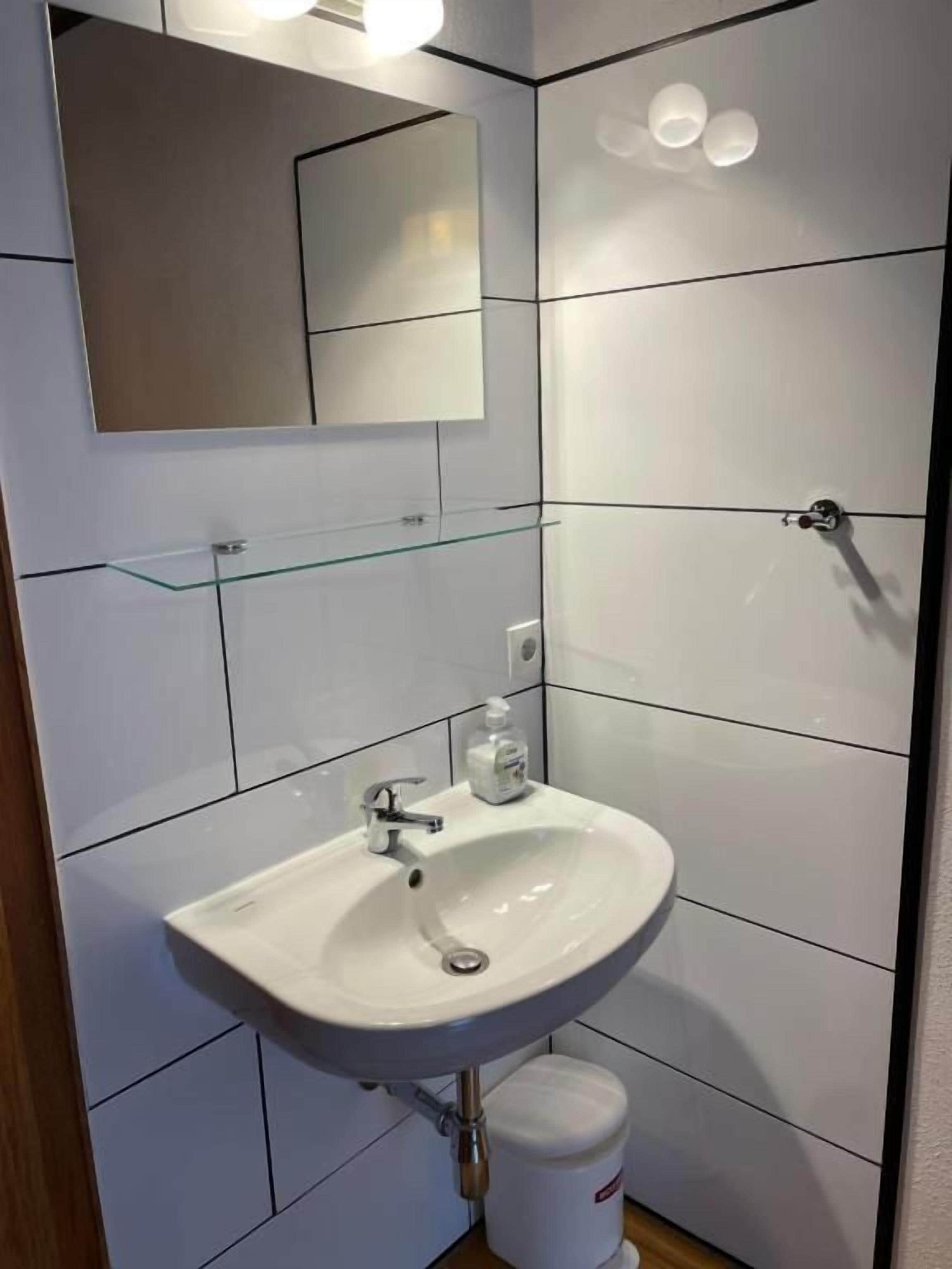 A bathroom with a white sink, a glass shelf, a mirror, and a toilet.