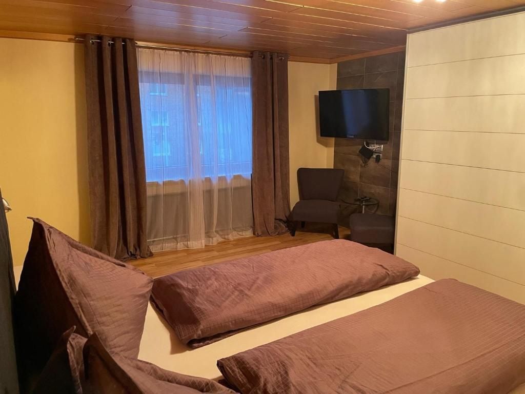 A room with a bed, a chair, a television, and a window with curtains.