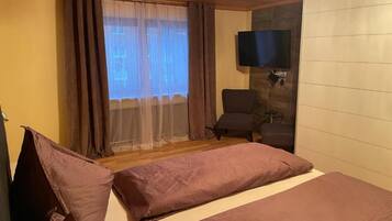 Ein Zimmer mit einem Bett, einem Sessel, einem Fernseher und einem Vorhangfenster.