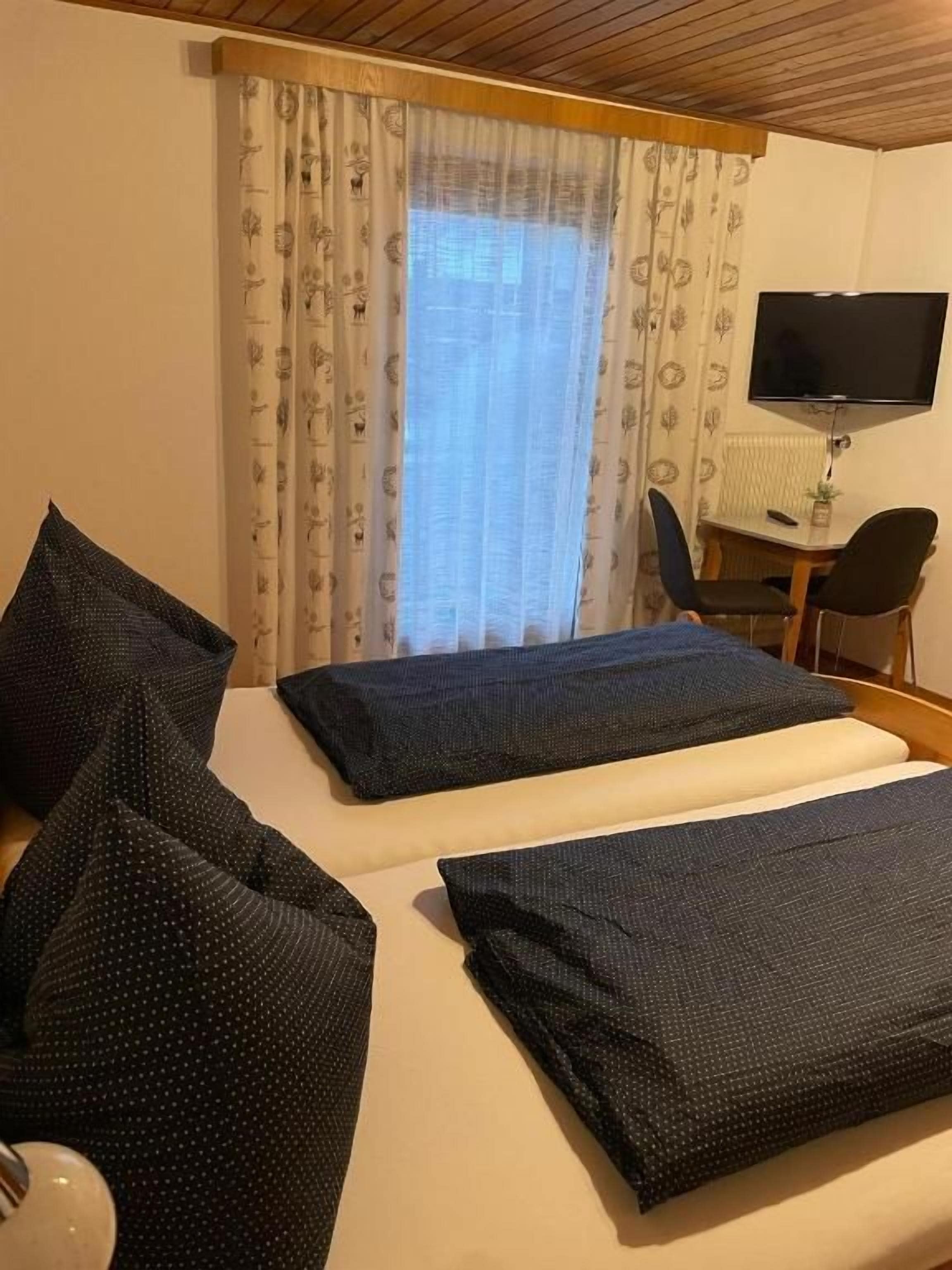 A hotel room with a bed, two pillows, a TV, a desk, and a chair.