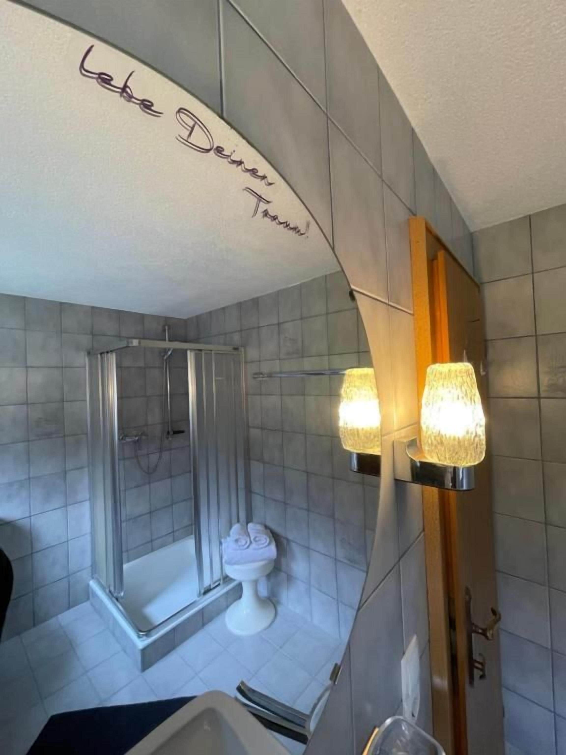 A bathroom with a shower, toilet, and a mirror with a handwritten message.