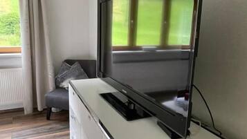 A modern living room with a flat-screen TV mounted on a cabinet, a remote control, and a window with curtains.