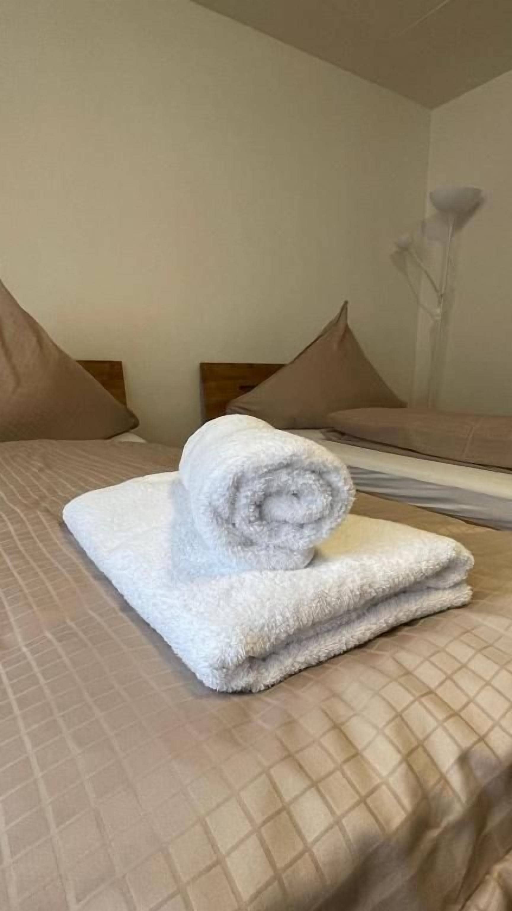 Una habitación de hotel con una cama, almohadas y una toalla enrollada sobre la cama.