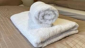 Una habitación de hotel con una cama, almohadas y una toalla enrollada sobre la cama.