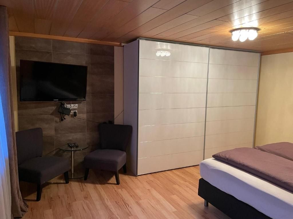 Une chambre à coucher comprenant un lit, un téléviseur fixé au mur, une armoire et deux chaises.