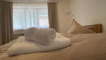 A hotel room with a bed, a window with curtains, and a wall-mounted lamp.