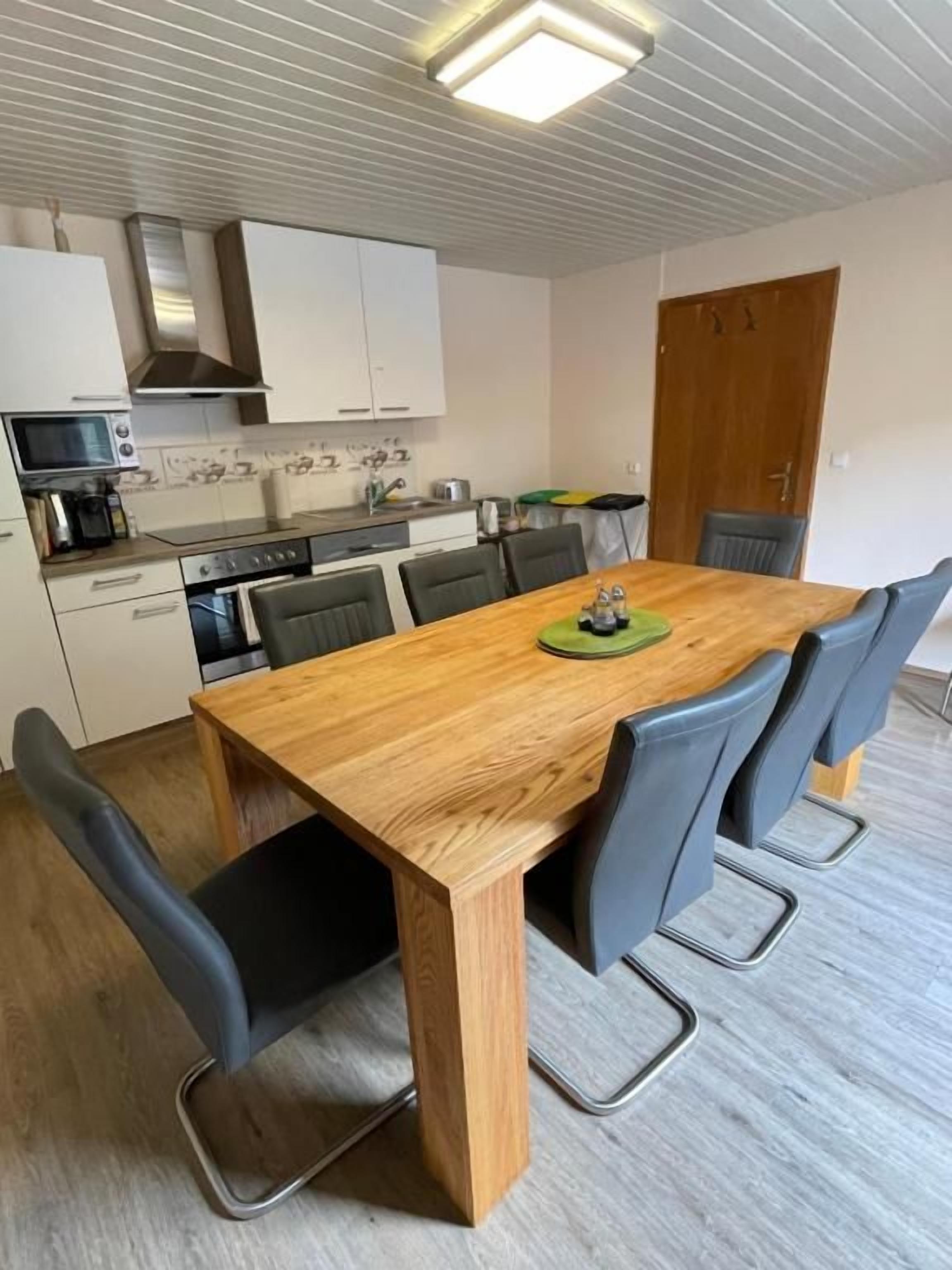A compact kitchen with white cabinets, a microwave, and a stove. There is a wooden dining table with four chairs.