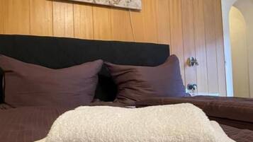 A bed with a dark headboard, a white fluffy pillow, and a brown patterned bedspread.