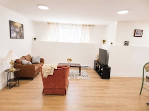 A living room with a brown sofa, a red armchair, a coffee table, a TV stand, and a lamp.