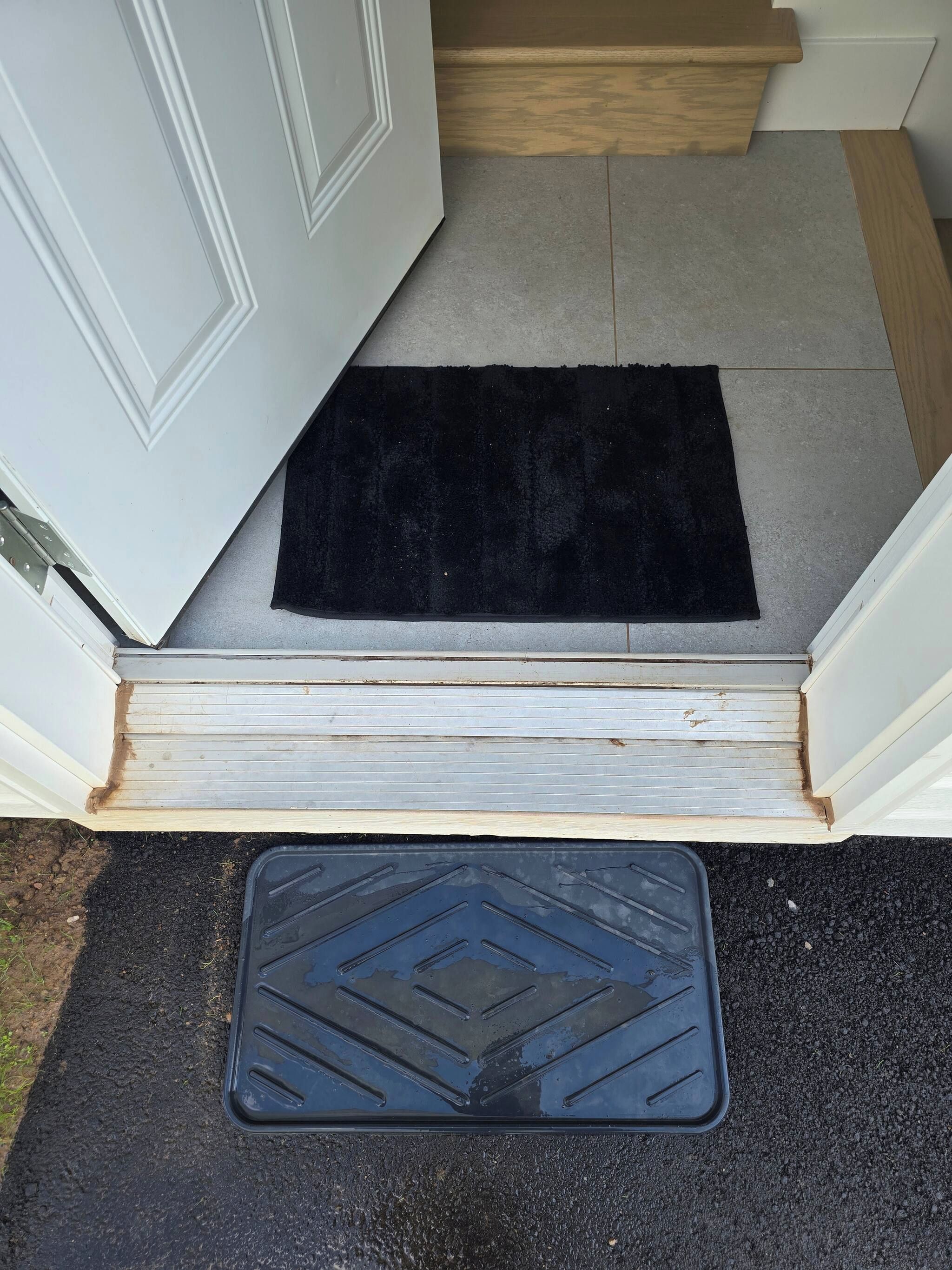 A set of steps leading to a door with a black doormat and a black mat with diamond patterns on the ground.