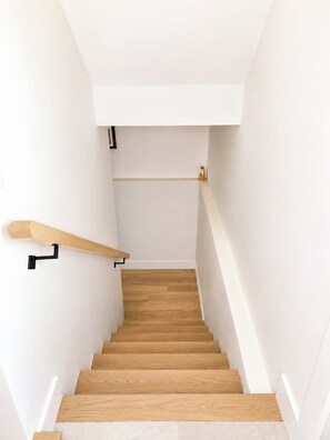 A staircase with wooden steps and a handrail, leading to a landing with a light switch and a small object on the wall. - Your Peaceful Cocoon at the Gates of Downtown (Riverview)