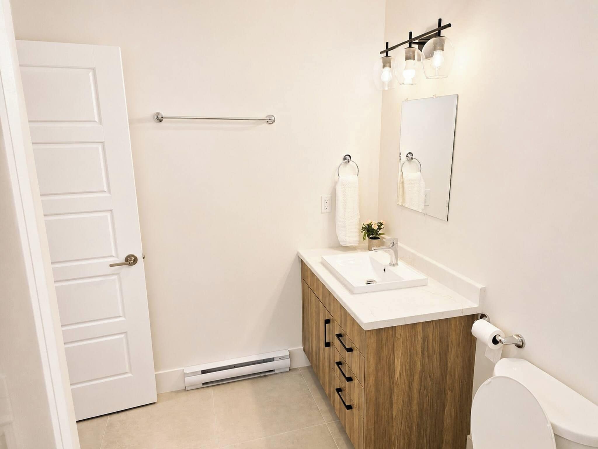 Une salle de bain avec une porte blanche, un meuble-lavabo en bois, un évier, des toilettes, un porte-serviettes, un miroir et une serviette.
