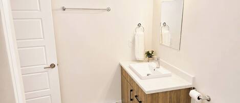 Une salle de bain avec une porte blanche, un meuble-lavabo en bois, un évier, des toilettes, un porte-serviettes, un miroir et une serviette.