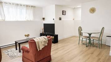 Un salon comprenant un canapé, un téléviseur, une table à manger avec des chaises et un petit tapis.