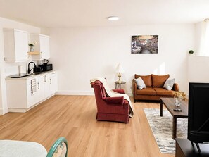 A modern living space with a kitchen, a red armchair, a brown sofa, and a painting on the wall. - Your Peaceful Cocoon at the Gates of Downtown (Riverview)