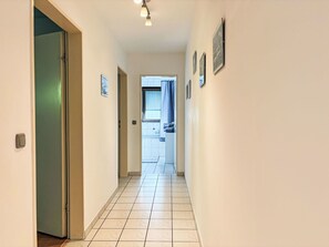 Ein Flur mit gefliestem Boden, der zu einem Badezimmer mit Fenster und Waschbecken führt.