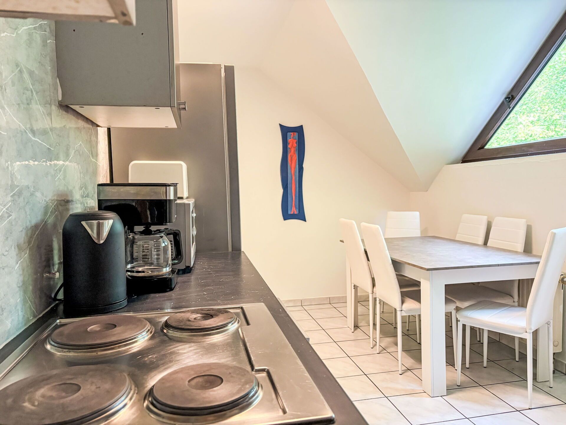 A kitchen with a stove, coffee maker, and a dining area with a table and chairs.