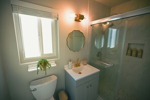 Een badkamer met toilet, wastafel, spiegel, douche en een raam met zonwering.