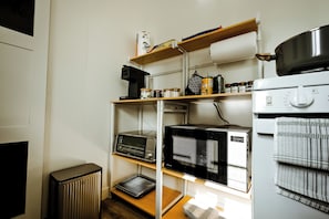 Una cocina compacta equipada con microondas, horno y estantes con utensilios de cocina.