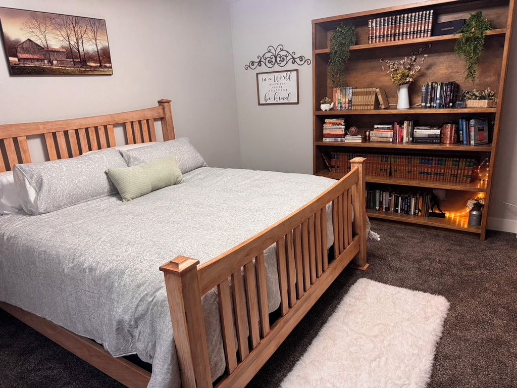 Une chambre à coucher avec un lit en bois, une bibliothèque et une citation encadrée accrochée au mur.