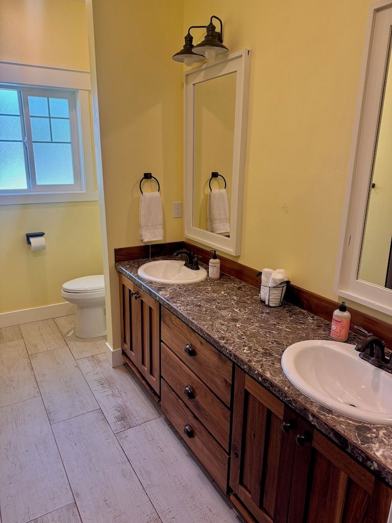 Une salle de bain avec deux lavabos, des meubles en bois, un miroir et des toilettes.