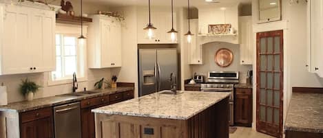 A kitchen with a central island, stainless steel appliances, pendant lighting, and wooden cabinetry.