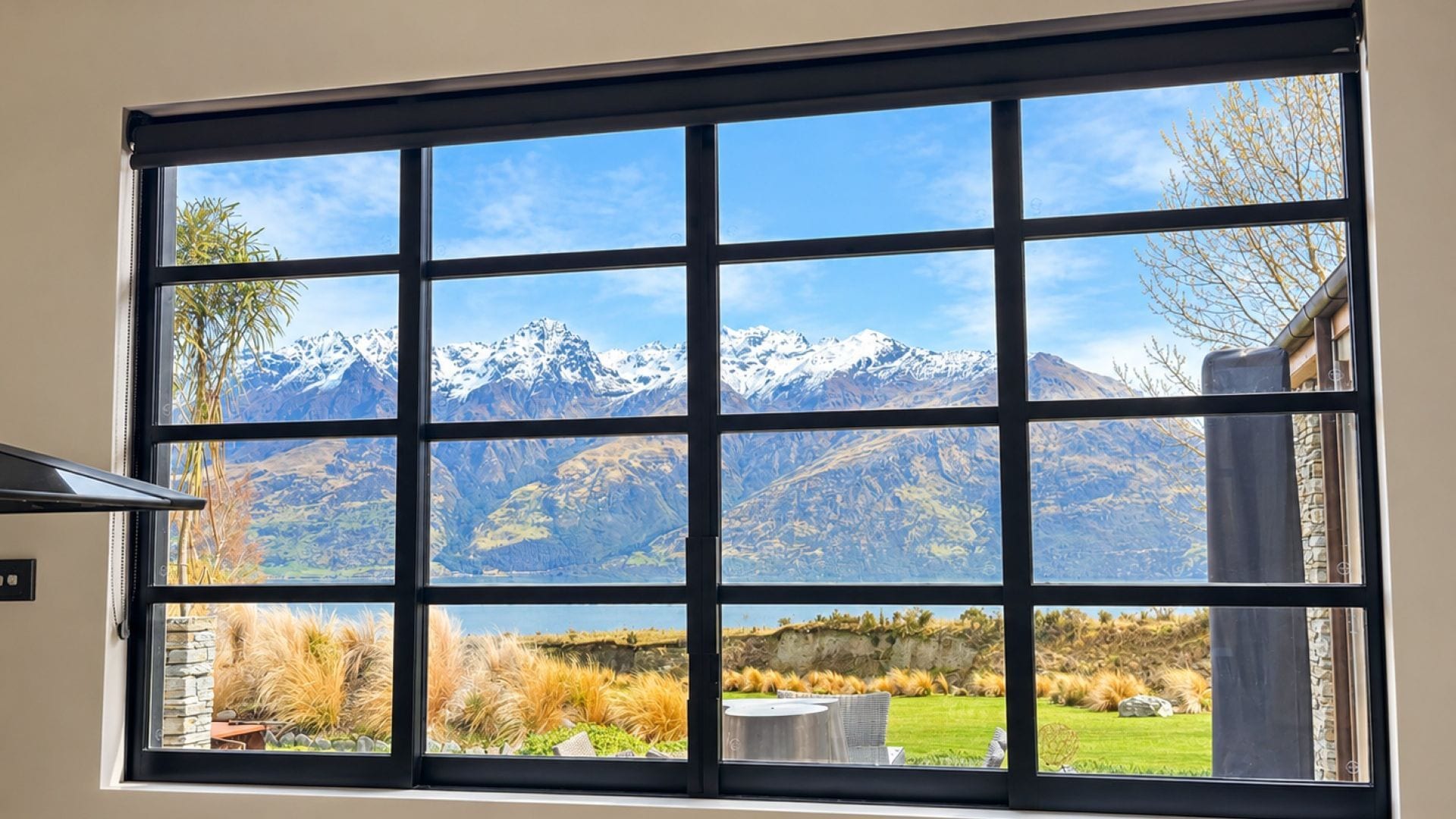 Ein großes Fenster mit Blick auf eine gebirgige Landschaft und einen darunterliegenden Garten.