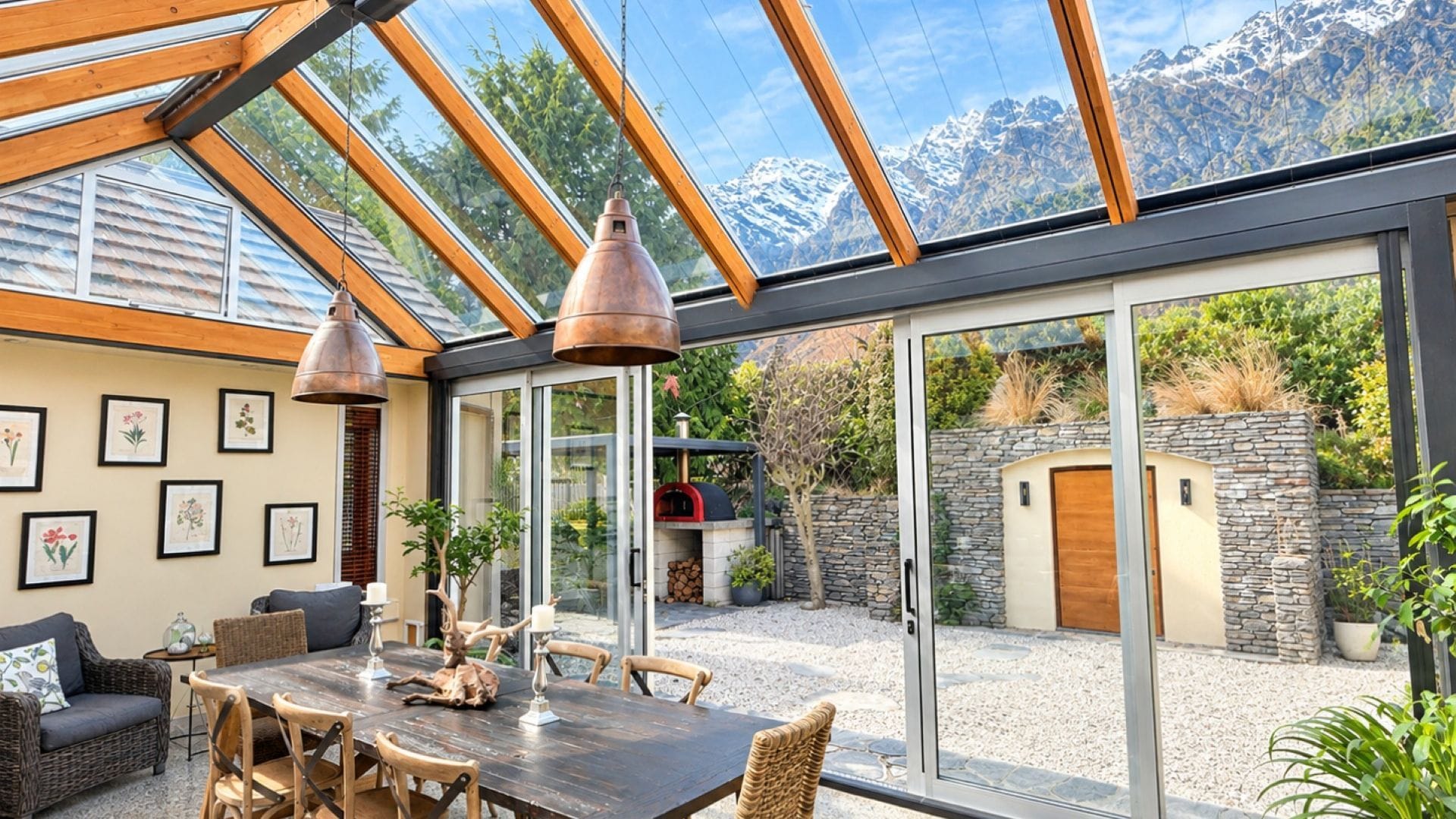 Een moderne buiten eethoek met een glazen overkapping, houten meubels en uitzicht op de bergen.