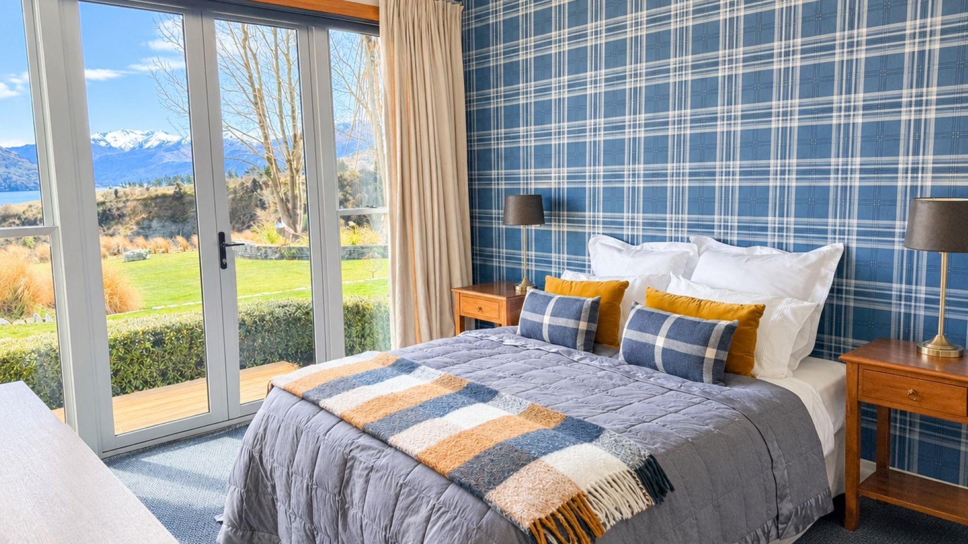 A bedroom with a large bed, a view of mountains through a sliding door, and a plaid-patterned wall.