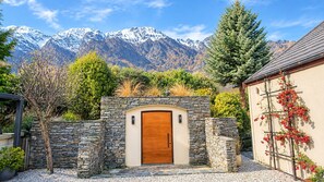 A stone-walled entrance with a wooden door, surrounded by a gravel driveway, with a mountain backdrop. - The Tussocks at Drift Bay (Drift Bay)