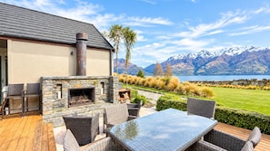 A stone fireplace with a chimney, outdoor furniture, and a view of mountains and a lake. - The Tussocks at Drift Bay (Drift Bay)