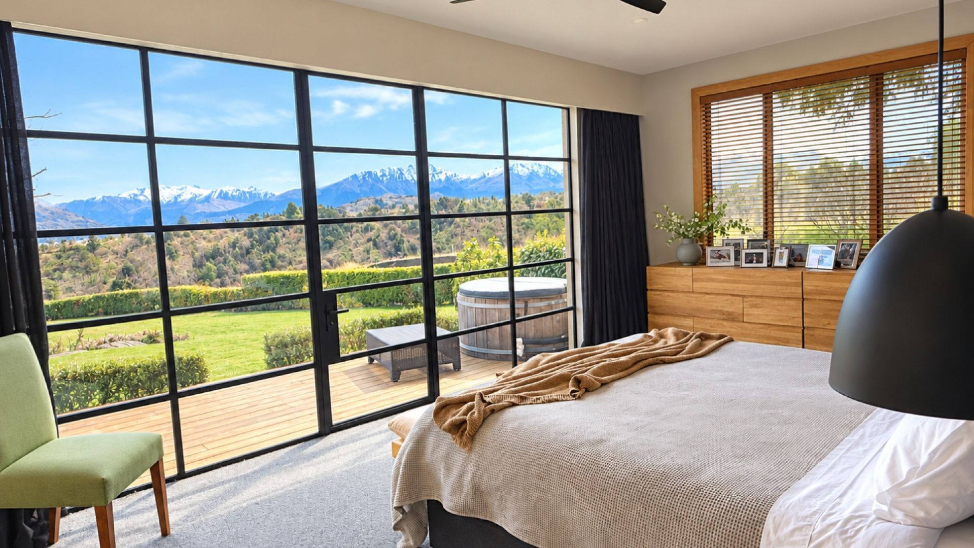 Un dormitorio con un ventanal grande, una cama, un sillón y un aparador de madera.